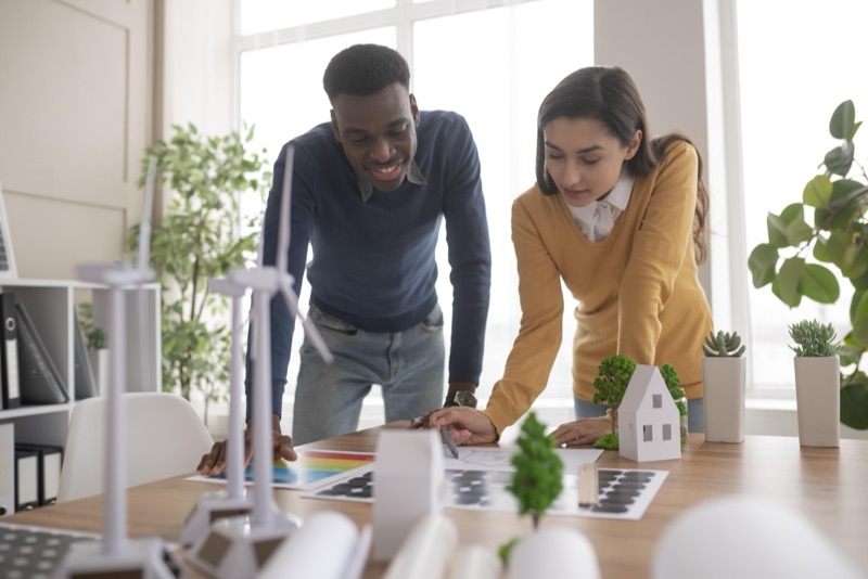 Two people study documents and a house model on a desk